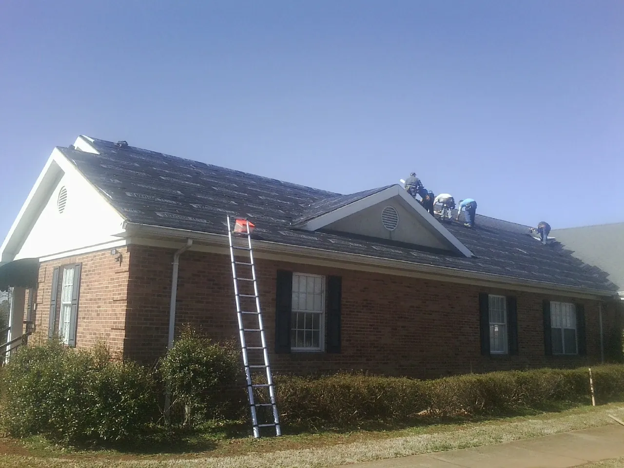 Crew tearing shingles off a brick ranch roof with a ladder set — Emergency Roof Repair work by our crew in Dunkirk