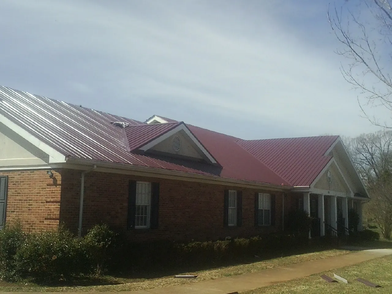 Red metal roof with gabled entries on a long brick building, from a Hail Damage Roof Repair job in Dunkirk