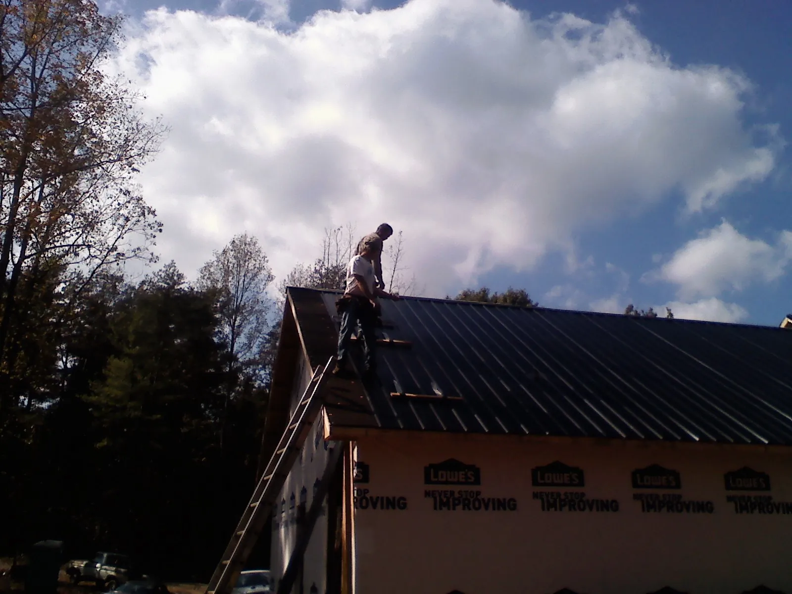 Roofer fastening dark metal panels high against a cloudy sky, from a Roof Inspection job in Dunkirk