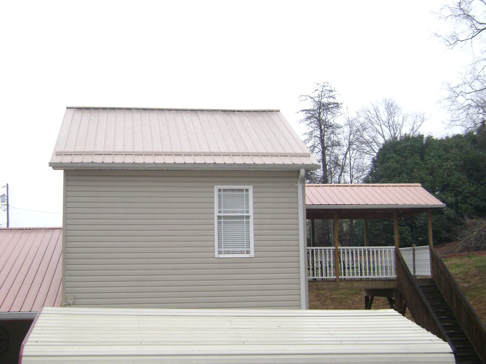 Tan metal roofs on a two story addition and attached porch, from a Roof Replacement job in Dunkirk